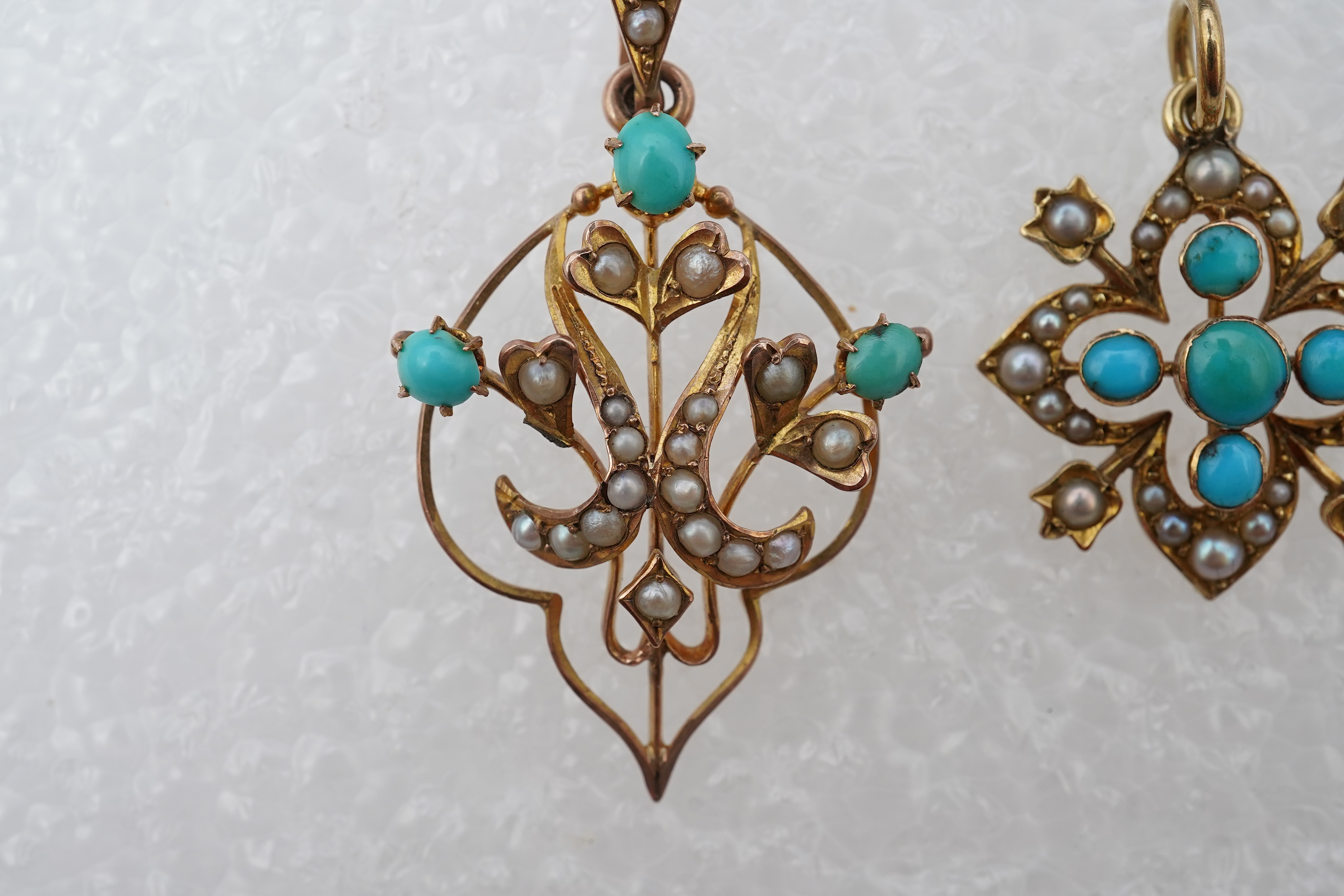 Two Edwardian turquoise and seed pearl pendants, each of foliate design, set with turquoise cabochons and seed pearls, mounted in gold, longest 3.7cm, smaller stamped 15CT, combined gross weight approximately 4 grams